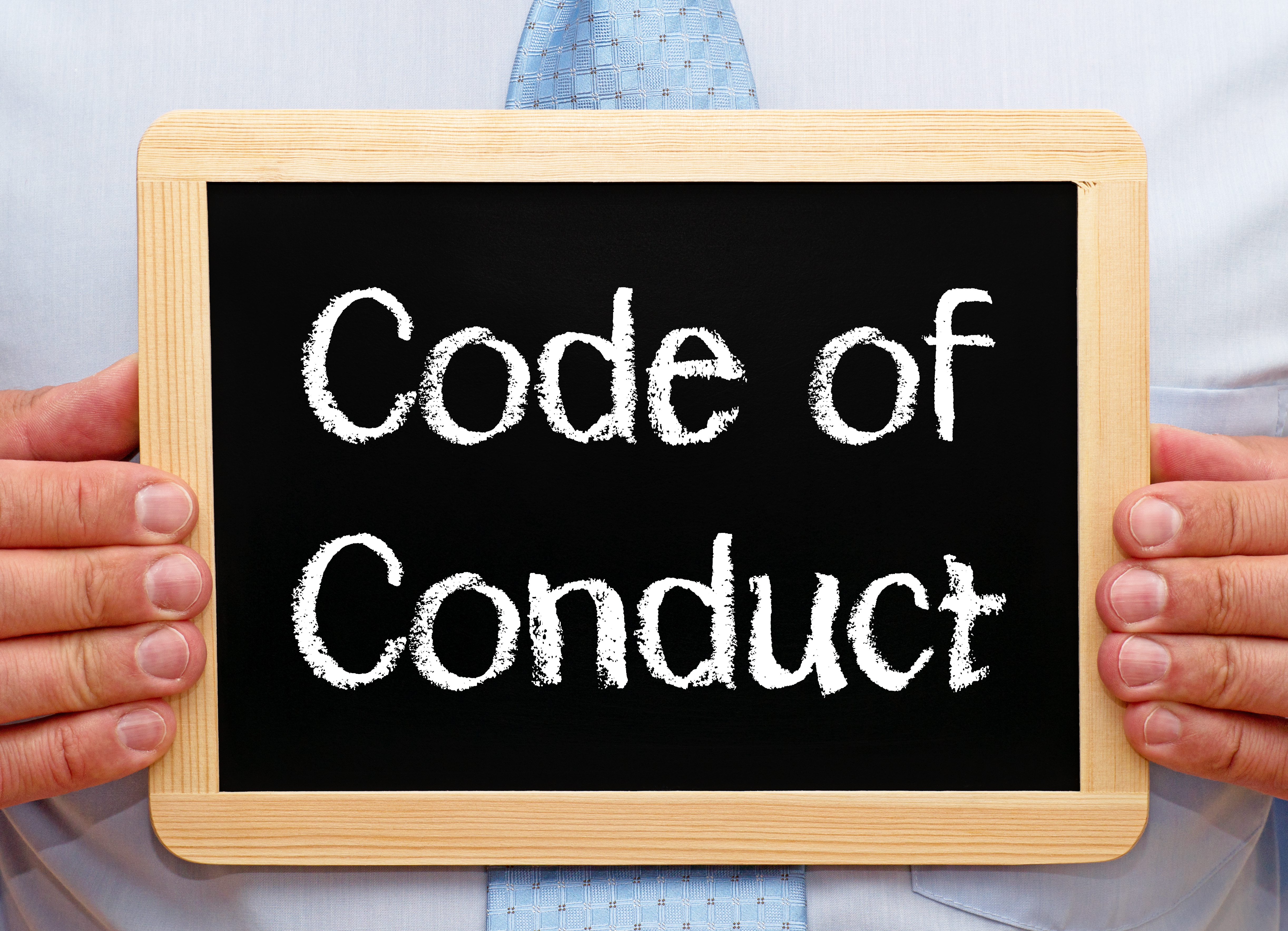 Hands holding chalkboard, text reads 'Code of Conduct' 