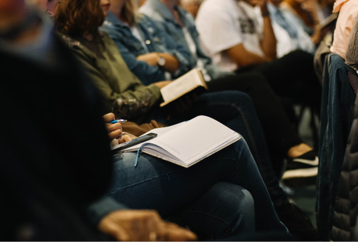 Photo of people sitting cross-legged with notebooks on their knees at a lecture, by Sincerely Media on Unsplash