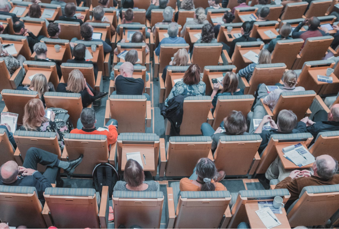 From behind lots of people sitting in a lecture theatre by Mikael Kristenson on Unsplash